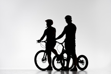 silhouettes of trial bikers in helmets with bicycles on white
