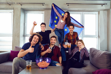A group of friends with a European flag at a party. Friends with cup of beer celebrate the day of Europe.