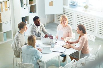Multi-ethnic team of managers gathered together at spacious open plan office and discussing start-up project, high angle view