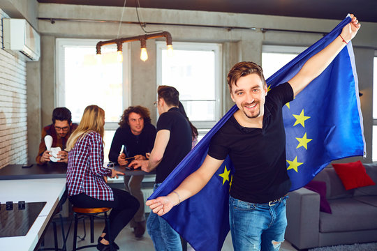 Young man with the european flag in his hands on the background of friends in the room.