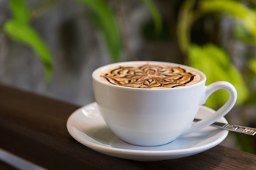Latte art coffee cup with blur of plants on wood