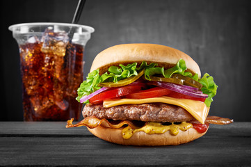 Beef burger with bacon and Cola cup drink on wooden table isolated on black background.