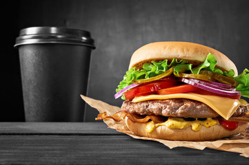 Beef burger with bacon and coffee cup drink on wooden table isolated on black background.