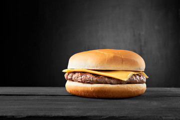 Plain beef burger with cheese on wooden table isolated on black background. - obrazy, fototapety, plakaty