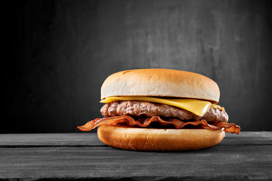 Plain beef burger with bacon and cheese on wooden table isolated on black background.