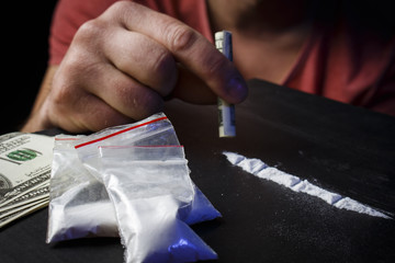 Drug addict man using narcotics, sniffing cocaine lines white powder with rolled dollar banknote