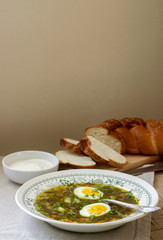 Vegetarian sorrel soup with egg, served with sour cream and bread. Rustic style.