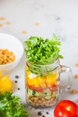 Salad in a jar. Homemade healthy salad from chickpea, tomato, yellow paprika, cucumber and green lettuce