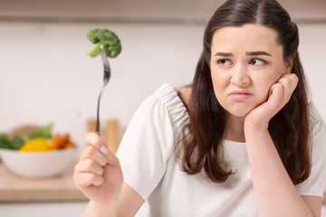 Vegetable diet. Sad dull woman holding broccoli on fork while making grimace