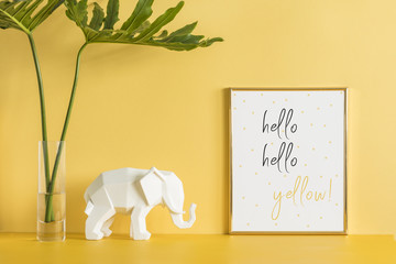The creative yellow desk with leafs, elephant and poster frame. Modern office work space..