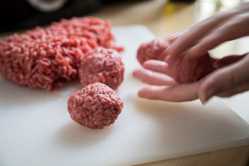 Weibliche Hände rollen Hack aus Rind und Schwein zu Bällchen