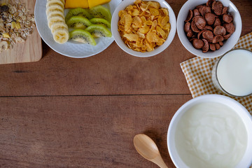Healthy breakfast with yogurt, Corn cereal, chocolate cereal, fresh fruits, muesli and milk on wooden background. Diet eating. Top view and copy space