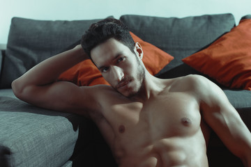 sexy and naked muscular young man posing on the floor near the sofa