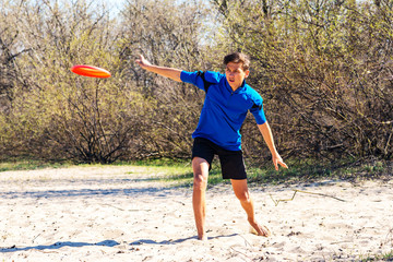 Athletic teenage boy is enthusiastically throwing frisbee disk