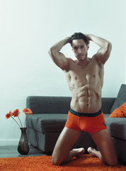 sexy and naked muscular young man posing on the floor near the sofa