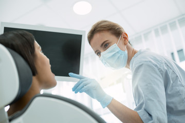 Open your mouth. Concentrated experienced dentist wearing a mask and examining her patients teeth