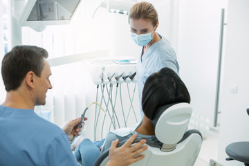 Dental work. Inspired skilled dentist wearing a mask and looking at her patient