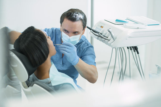 Small cavity. Concentrated dark-haired dentist wearing a uniform and examining his patients teeth