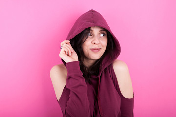 Surprised woman with a hood on her head on pink background in studio