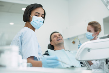 Obraz premium Our usual work. Concentrated skilled dentist wearing a mask and the patient sitting in the chair