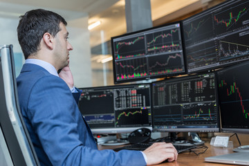 Male stock broker trading online watching charts and data analyses on multiple computer screens.