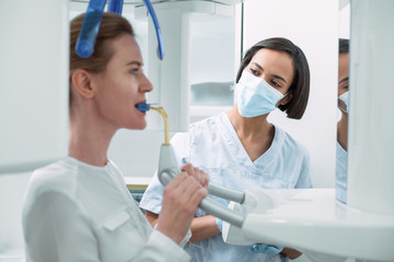 Under control. Alert experienced dentist wearing a uniform and watching her patient