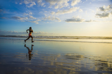 silhouette of young Asian sport runner woman in running workout training at sunset beach with orange sunlight reflection on the sea water