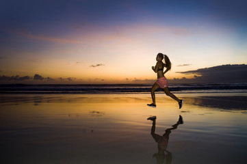 silhouette of young Asian sport runner woman in running workout training at sunset beach with orange sunlight reflection on the sea water