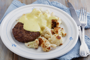 Meat burger with cauliflowers under cheese sauce