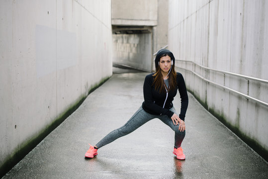 Sporty woman stretching and warming up legs for running urban fitness workout. Sport and healthy lifestyle concept. Female athlete exercising outside.
