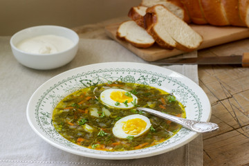 Vegetarian sorrel soup with egg, served with sour cream and bread. Rustic style.
