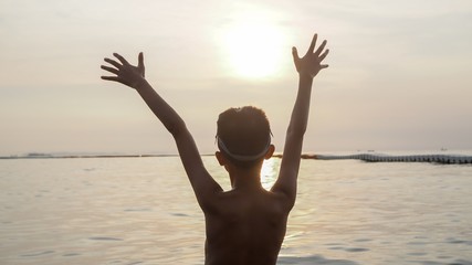 Asian boy raised his arm into the air by the sea.