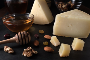 Greek cheese graviera and a slices on black stone board with nuts, honey and herbs.