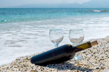 Bottle of red wine with wine glasses on the beach at the summer sunny day. Sea on the background.