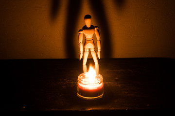 wooden doll on a black background in the light of a candle in a jar