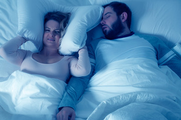 Man snoring and woman can't sleep, covering ears with pillow for snore noise
