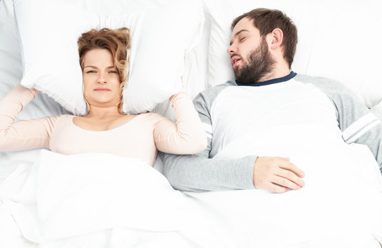 Man Snoring And Woman Can't Sleep, Covering Ears With Pillow For Snore Noise