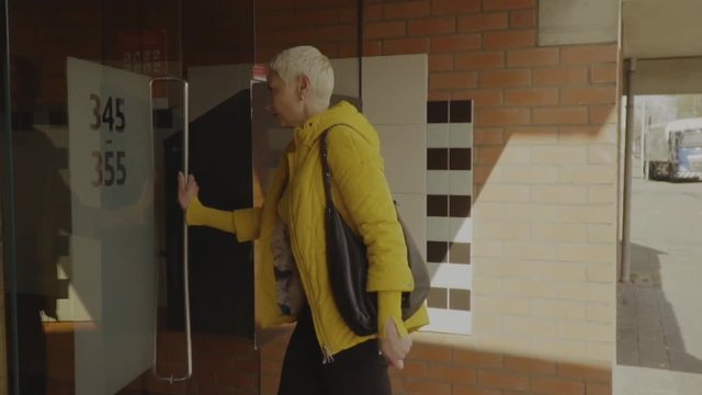 Happy woman using intercom at building entrance 