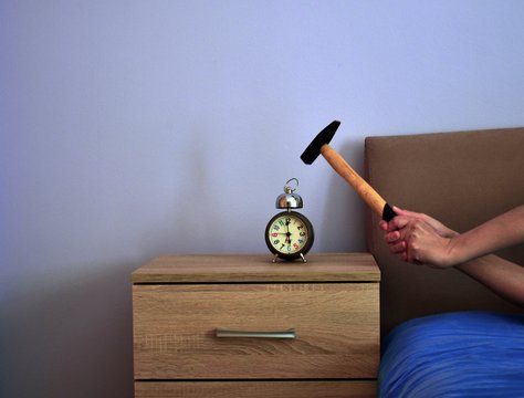 Image shows hands holding a hammer trying to smash an alarm clock.