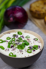 Bowl with curd decorated with spring onion. Baked jacket potatoes and spring onion on the background