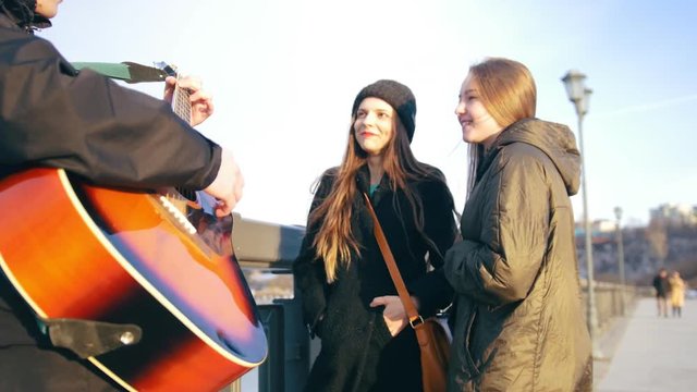Young girls having fun while guy playing on the guitar outdoors