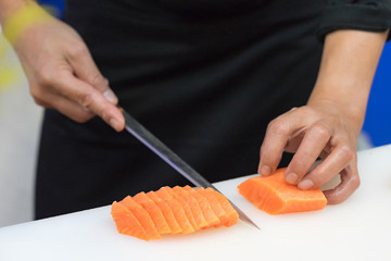 Hand of chef use knife preparing a fresh salmon on a cutting board, Japanese chef in restaurant slicing raw salmon, ingredient for seafood dish