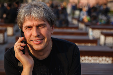 Portrait of Mature Handsome Man with smartphone looking at camera and smiling. Happy adult man with grey hair and white teeth smile. Senior man with mobile phone