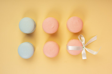 Blue and pink pastry macaroons, one of which is tied with a ribbon with a bow, arranged on a yellow background