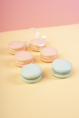 Blue and pink pastry macaroons, one of which is tied with a ribbon with a bow, arranged on a yellow and pink background