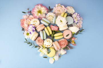 Multi сolored macaroons cakes with big and small different flower buds lay out in the shape of a heart on a blue background