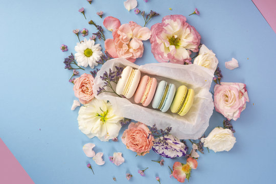 Multicolored macaroons cakes with big and small different flower buds in a gift box with wrapping paper on a blue and pink background
