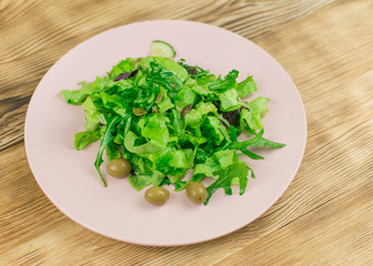 Fresh lettuce leaves, basil, arugula in a glass bowl on a wooden background. Preparation of a vegetarian vegetable salad.