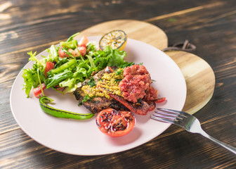 Grilled meat and salad of fresh vegetables on a plate on a wooden background.