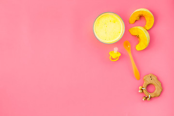 Healthy food for little baby. Puree with pumpkin near pacifier and toys on pink background top view copy space